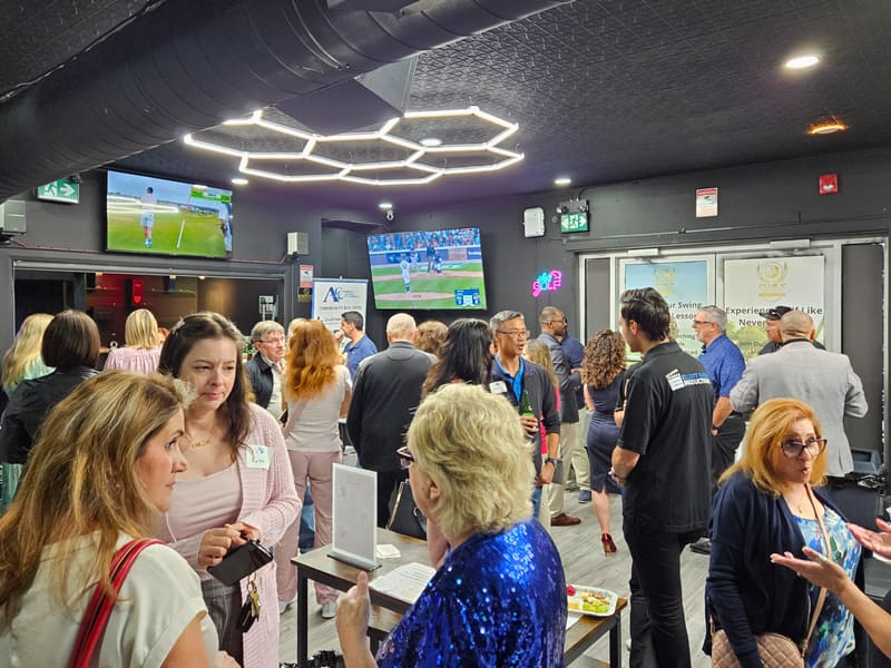 Wide view of a corporate event at Club X Indoor Golf, Aurora — attendees networking under hex-lit ceiling with simulator screens visible at the back