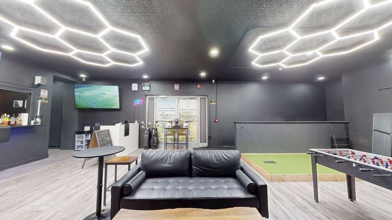 Club X Indoor Golf lounge in Aurora — wide view of the leather seating, simulator screen, and hex-lit ceiling